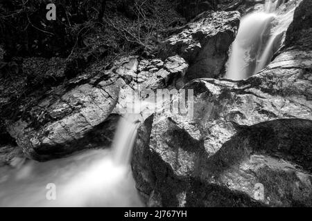 Ein kleiner Wasserfall in der Nähe von Kochel am See, am Fuße der bayerischen Alpen, stürzt zwischen großen Felsen hinab. Stockfoto