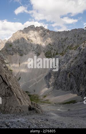 Blick durch die Viererscharte unterhalb der Viererspitze (2054m) im Karwendel oberhalb von Mittenwald, zum bekannten Dammkar. Das raue Gebiet der Fels- und Steinwüste wird nur durch den blauen Himmel mit einigen Wolken aufgebrochen. Stockfoto