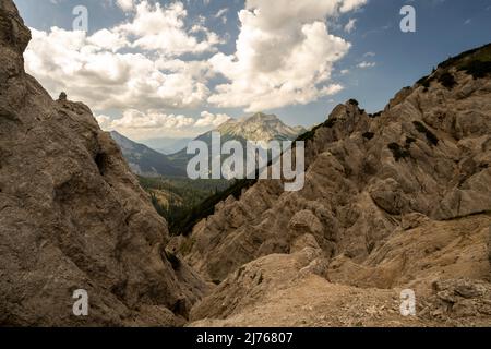 Auf dem Weg zwischen Rappenklammspitze und Wechselkopf gibt es mehrere freiliegende, rutschige Passagen mit dem typischen erodierten und exponierten Gelände des Karwendels. Rutschige Steine und felsige Kanten, im Hintergrund die Soierngruppe in den deutschen Voralpen. Stockfoto