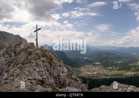 Die Viererspitze (2054m) im Karwendel bei der westlichen Karwendelspitze, oberhalb von Mittenwald im Werdenfelser Land, in den bayerischen Alpen. Das Gipfelkreuz ragt über dem Dorf, mit dem Kranzberg, Lautersee und Wetterstein im Hintergrund. Stockfoto