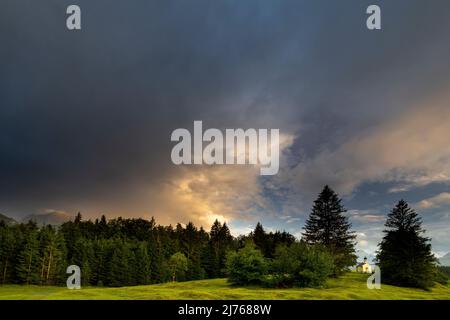 Die kleine Kapelle Maria Rast bei Gewitter und Sonnenuntergang, sehr winzig auf einem kleinen Hügel im Grünen. Stockfoto