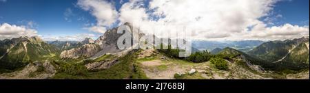 Panoramablick vom Wörnersattel bei Mittenwald im Karwendel, ncoh der bayerische Teil. In der Mitte thront der Wörner, ganz rechts und links die Soierngruppe. Die Sonne wird von einer Wolkenbank am sonst blauen Himmel versteckt. Stockfoto