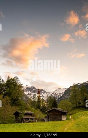 Alte Holzmühlen in Obernberg am Brenner, die historische Nikolaikirche im Hintergrund und Blumenwiesen im Vordergrund. Stockfoto