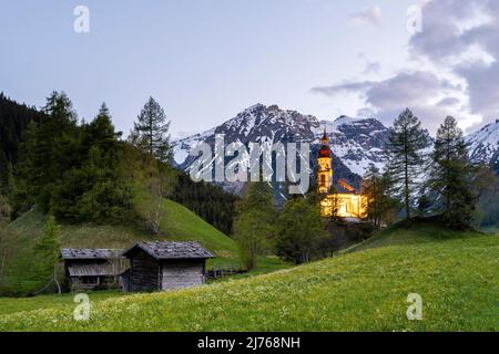 Alte Holzmühlen in Obernberg am Brenner, die historische Nikolaikirche im Hintergrund und Blumenwiesen im Vordergrund. Stockfoto