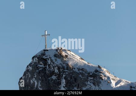 Das eingeschneite Gipfelkreuz der Westlichen Karwendelspitze im Karwendel oberhalb von Mittenwald, nahe der Bergstation der Karwendelbahn. Das Kreuz ist teilweise vereist, im Hintergrund der blaue Himmel. Stockfoto