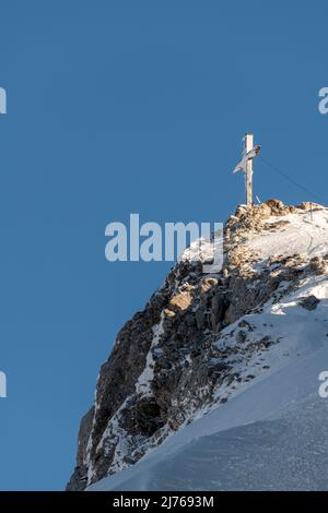 Das eingeschneite Gipfelkreuz der Westlichen Karwendelspitze im Karwendel oberhalb von Mittenwald, nahe der Bergstation der Karwendelbahn. Das Kreuz ist teilweise vereist, im Hintergrund der blaue Himmel. Stockfoto