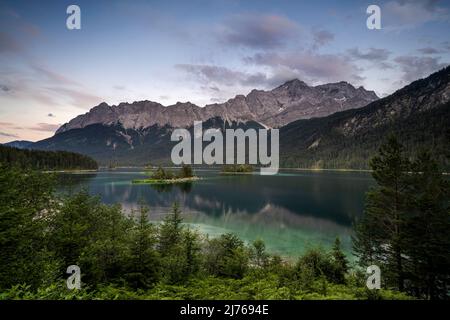 Der Eibsee und das Zugspitz-Massiv nach Sonnenuntergang mit sanften Farben und im Vordergrund der See mit seinen kleinen Inseln. Stockfoto