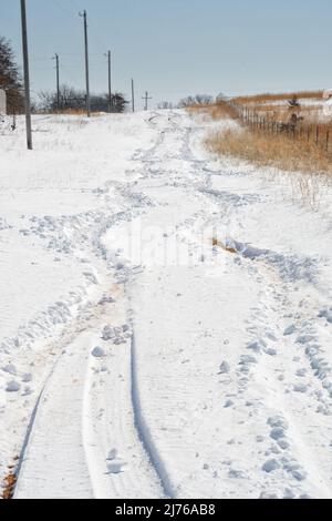 Schwankende Reifenspuren, die von einem Fahrzeug hinterlassen wurden, das nach einem Schneesturm in tiefem, unbepflügten Schnee bergauf kämpfen muss Stockfoto