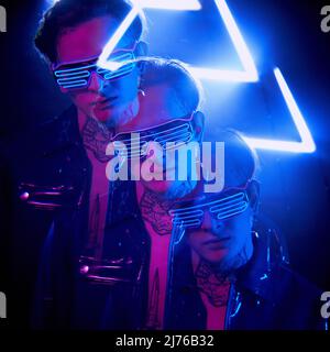 Stroboskopisches Foto eines futuristischen jungen Mannes mit Tattoo am Hals, der in Neonlicht auf einem Dreieck steht Stockfoto