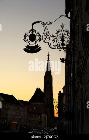 Deutschland, Bayern, Oberbayern, Altötting, Neuötting, Stadtplatz, Ludwigstraße, Pfarrkirche St. Nikolaus, Häuserzeile, schmiedeeisernes Zunftschild, Dämmerung, Silhouette Stockfoto