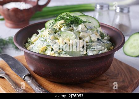 Salat mit Gurken, gekochten Eiern, Schnittlauch und Kräutern in brauner Schüssel auf Holzbrett Stockfoto