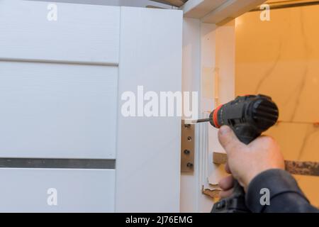 Anbringen des Türscharniers am Türrahmen mit einem Schraubendreher Stockfoto