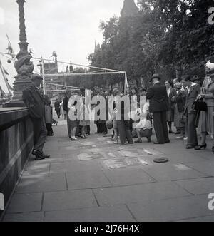 1953, historisches Großbritannien der Nachkriegszeit und eine kleine Menge von Erwachsenen und Kindern, die einem Straßenpflaster-Künstler bei der Arbeit zusehen, Embankment, London, England, Großbritannien. Stockfoto