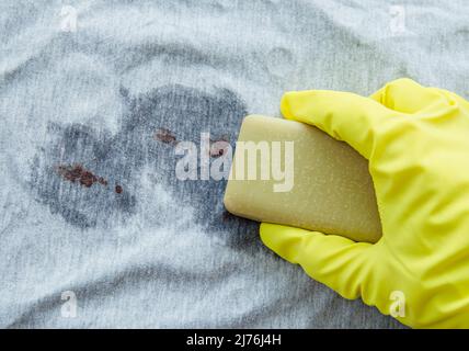 Entfernen von Blutflecken mit einem Seifenstück aus Galle (Galle, saft). Konzept für natürliche, chemikalienfreie Haushaltskleidung für Waschprodukte. Seifenstück in der Hand. Stockfoto