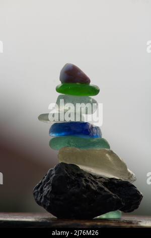 Nahaufnahme von Glassteinchen und einer winzigen Meeresmuschel, die auf einem Lavastein balanciert Stockfoto