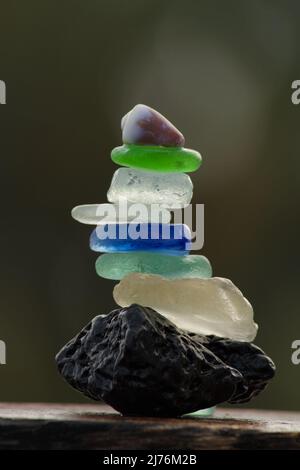 Nahaufnahme von Glassteinchen und einer winzigen Meeresmuschel, die auf einem Lavastein balanciert Stockfoto