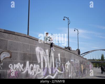 Ein junger Mann an einer Wand genießt die Sonne und blickt auf den Frankfurter Hafenpark Stockfoto