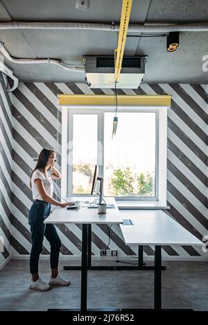 Steharbeitsplatz. Im Stehen arbeiten. Stehtisch für die Arbeit von zu Hause oder im Büro. Junge Programmiererin, die im Stehen arbeitet Stockfoto