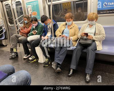 Die New Yorker fahren in Brooklyn mit Masken und Telefonen in einem U-Bahn-Zug. Stockfoto