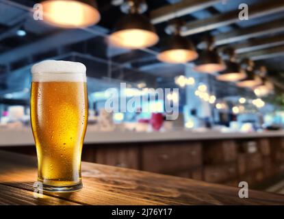 Gekühltes Glas Bier auf dem Holztisch. Unscharfer Barinnenraum im Hintergrund. Stockfoto