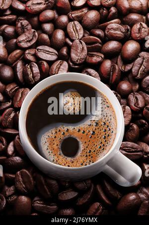 Tasse Kaffee americano über gerösteten Kaffeebohnen. Symbol Yin und Yang aus Schaum gebildet. Stockfoto