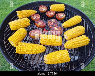 Ähre von Mais oder Mais und Tomaten auf dem Grill. Foto von Gemüse auf dem Grillrost. Kochvorgang. Stockfoto