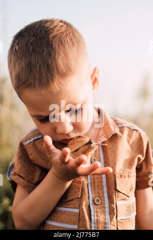 Ein ernsthafter kleiner Junge hält in der Natur eine Schnecke in der Hand Stockfoto