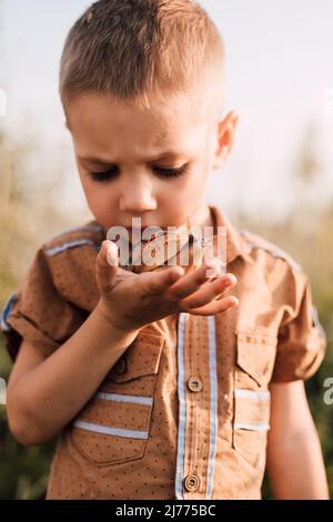 Ein ernsthafter kleiner Junge hält in der Natur eine Schnecke in der Hand Stockfoto