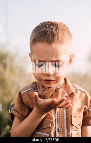 Ein ernsthafter kleiner Junge hält in der Natur eine Schnecke in der Hand Stockfoto