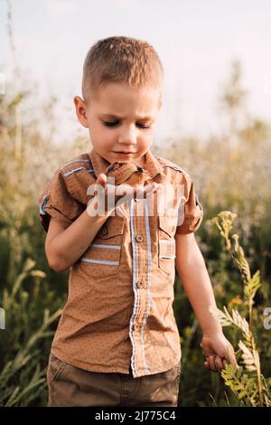 Ein ernsthafter kleiner Junge hält in der Natur eine Schnecke in der Hand Stockfoto