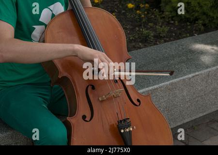 Detail eines Mannes, der das Holzcello spielt und die Saiten mit dem Bogen reibt, um die Noten eines klassischen Musikstücks zu erhalten. Stockfoto