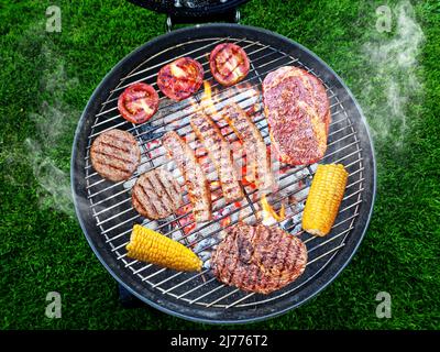 Gegrilltes Fleisch, Würstchen und Gemüse auf offenem Grillrost. Konzeptionelles Foto des Grillkochvorgangs. Stockfoto