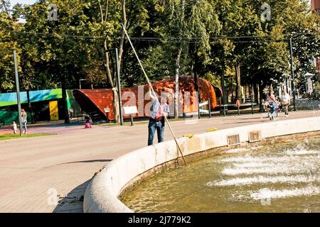 Dnipro, Ukraine - 09.13.2021: Reinigung von Brunnen in der Stadt. An einem sonnigen Tag reinigt ein Mann einen Brunnen in einem Park im Stadtzentrum. Stockfoto