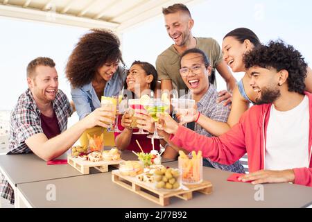 Multirassische junge Menschen, die Cocktails trinken. Freunde, die gemeinsam auf dem Dach Cocktails toasten. Lifestyle-Konzept für soziale Treffen Stockfoto