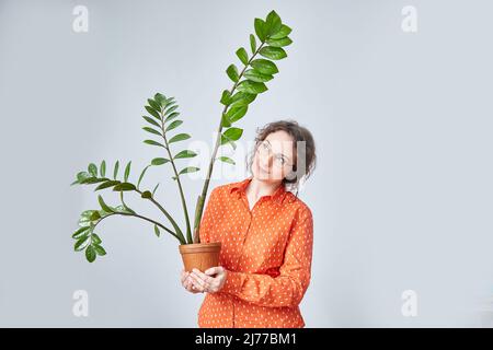 Eine Frau in leuchtend orangefarbenen Kleidern steht mit einem Blumentopf Stockfoto