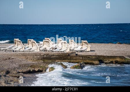 Leere Liegen und geschlossene Sonnenschirme am Strand in Griechenland. Stockfoto