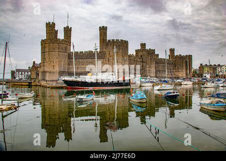 Perfekte Reflexion von Caernarfon Castle in der Menai Strait bei Ebbe, mit festgetäuten Booten, Caernarfon, Gwynned, Nordwales Stockfoto