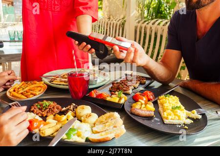 indischer Mann, der im Restaurant per Kreditkarte-App auf dem Smartphone-Reader bezahlt Stockfoto