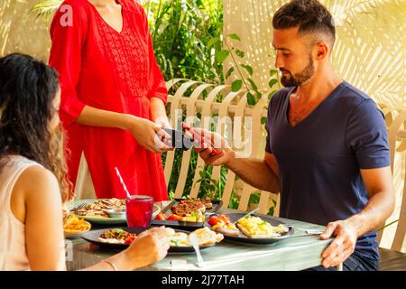 indischer Mann, der im Restaurant per Kreditkarte-App auf dem Smartphone-Reader bezahlt Stockfoto