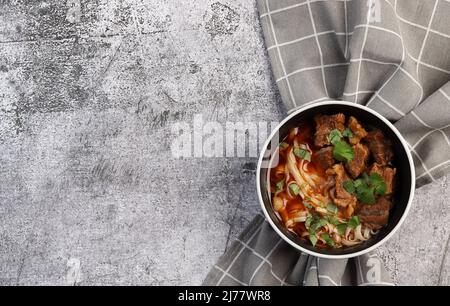 Würzige Rindernudelsuppe oder Ramen mit Kräutern in einer Schüssel auf dunkelgrauem Hintergrund. Draufsicht, flach liegend Stockfoto