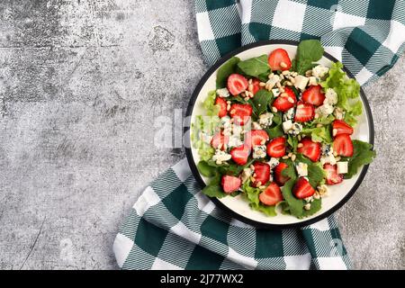 Blauer Käse- und Erdbeerarugula-Salat mit Pinienkernen auf einem runden Teller auf dunkelgrauem Hintergrund. Draufsicht, flach liegend Stockfoto