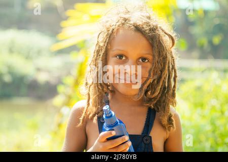 Mowgli indian Junge mit Dreadlocks Haare versteckt hält Mückenspray in Tropen grünen Wald Hintergrund Stockfoto