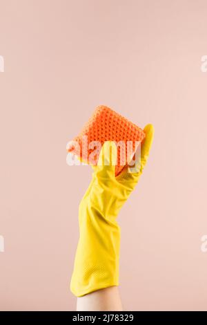 Hand in gelbem Handschuh hält Schwamm zum Spülen auf beigefarbenem Closeup-Kopierraum Stockfoto