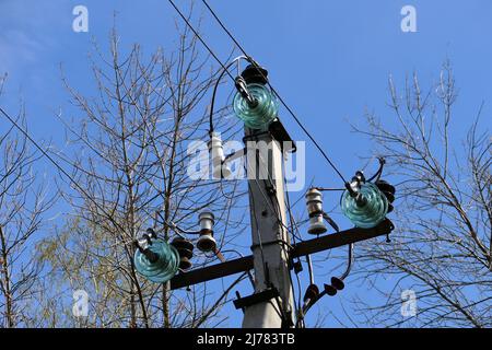 Nahaufnahme von Hochspannungsleitungen und Strommasten vor blauem Himmel. Stockfoto