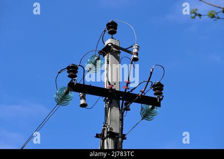 Nahaufnahme von Hochspannungsleitungen und Strommasten vor blauem Himmel. Stockfoto