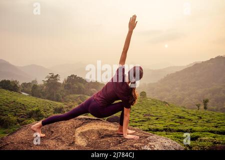 Frau in violettem Tuch, die Yoga auf Teeplantagen in Munnar Hill Kerala India macht Stockfoto