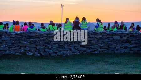 Menschenmengen beobachten den Sonnenaufgang nach der Dunkelheit in das Licht. Knockdrum Steinring Fort, West Cork, Irland Stockfoto