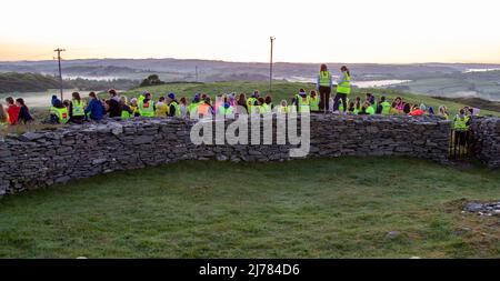 Menschenmengen beobachten den Sonnenaufgang nach der Dunkelheit in das Licht. Knockdrum Steinring Fort, West Cork, Irland Stockfoto