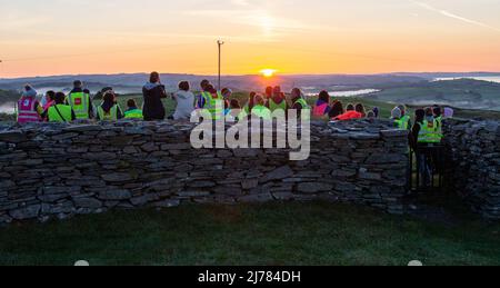 Menschenmengen beobachten den Sonnenaufgang nach der Dunkelheit in das Licht. Knockdrum Steinring Fort, West Cork, Irland Stockfoto