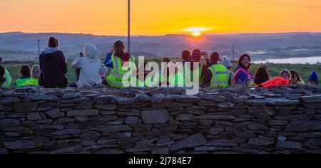 Menschenmengen beobachten den Sonnenaufgang nach der Dunkelheit in das Licht. Knockdrum Steinring Fort, West Cork, Irland Stockfoto